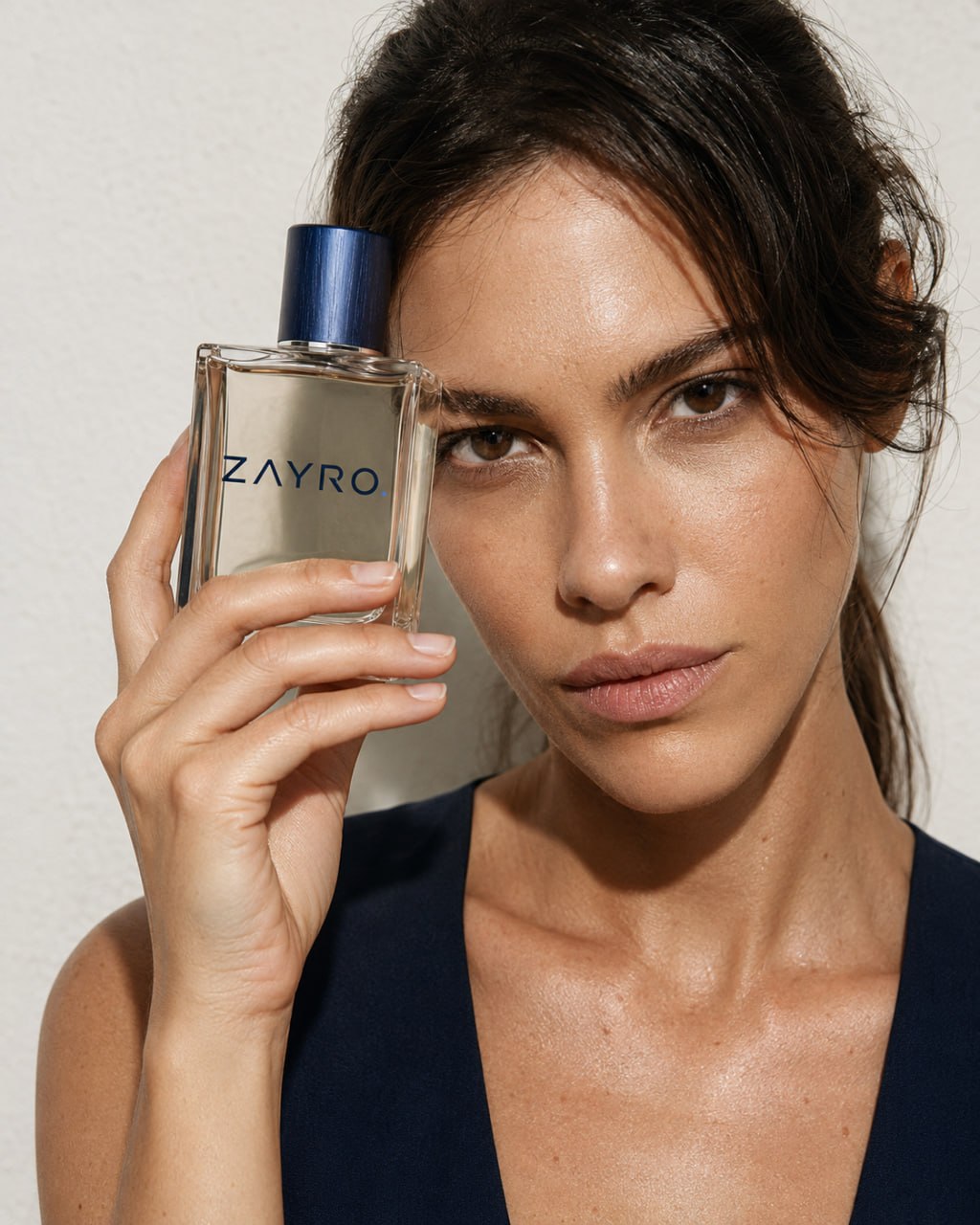 Woman holding a ZAYRO fragrance bottle beside her face