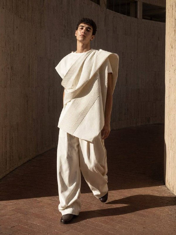 Male fashion model wearing sculptural ivory clothing in brutalist architecture