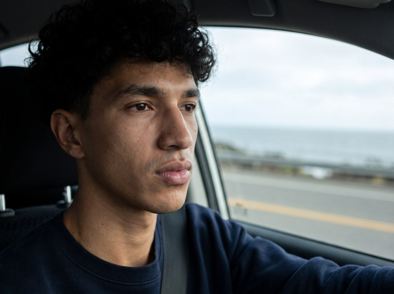 Young man driving beside the coast in a navy sweatshirt