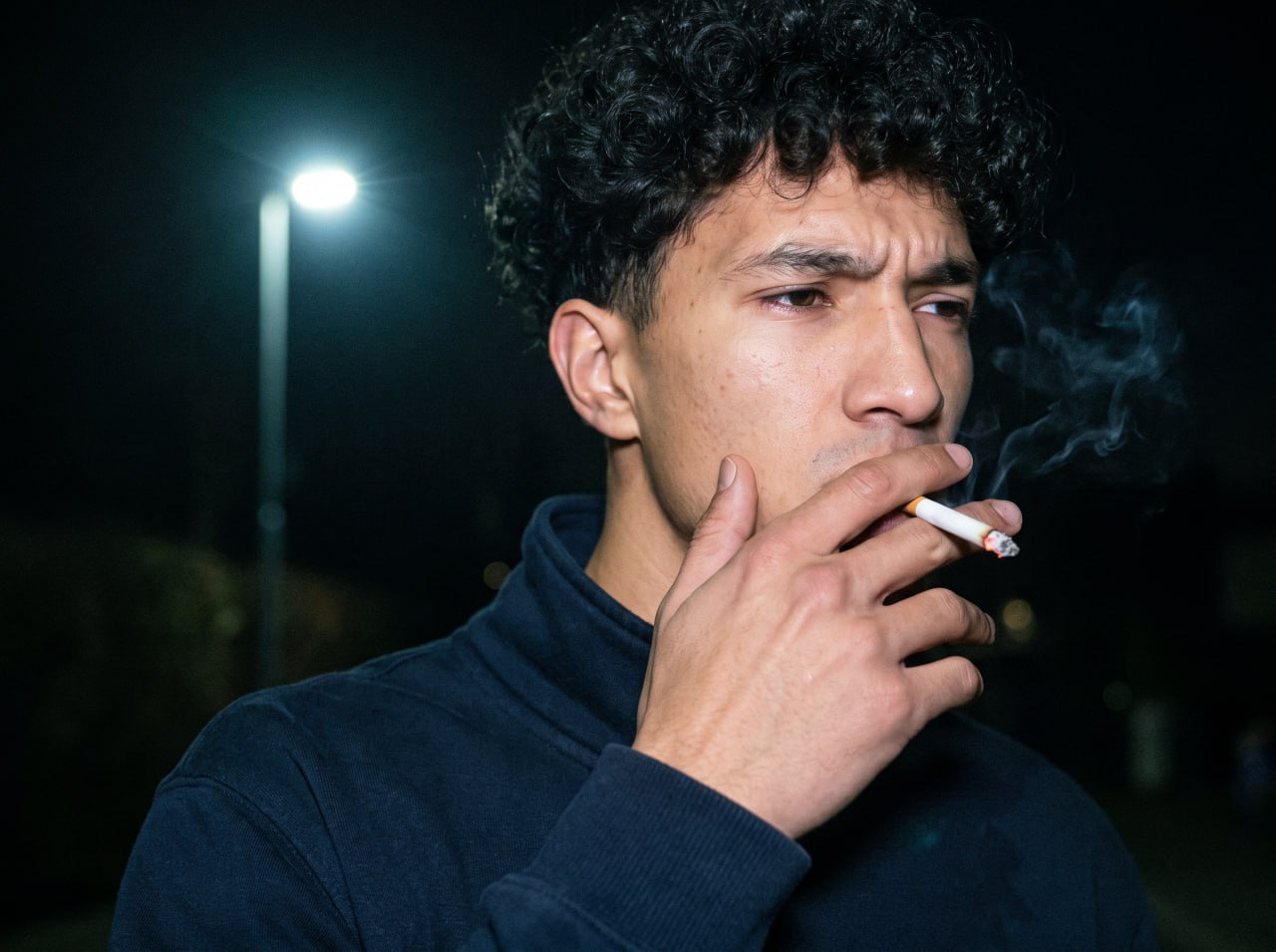 Flash-lit night portrait of a young man holding a cigarette