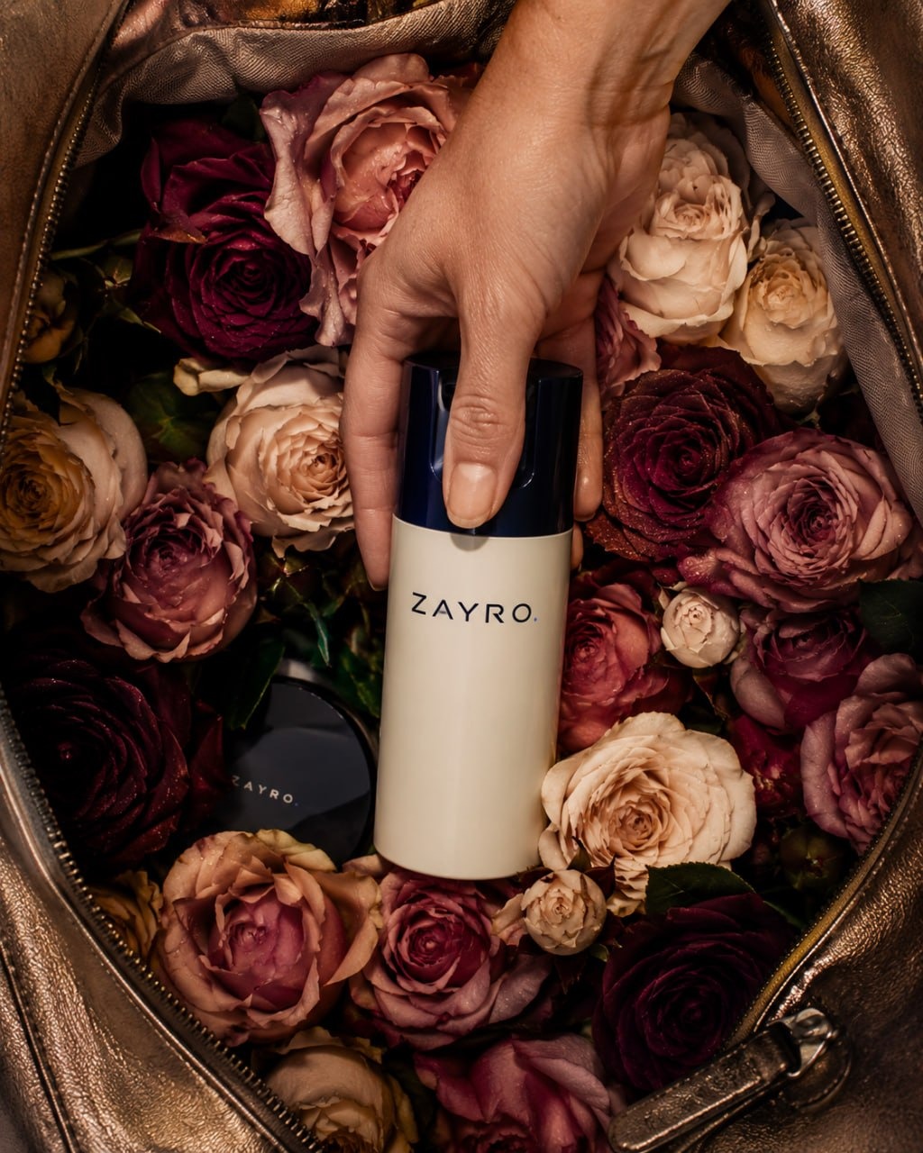 Hand lifting a ZAYRO beauty product from a flower-filled metallic bag
